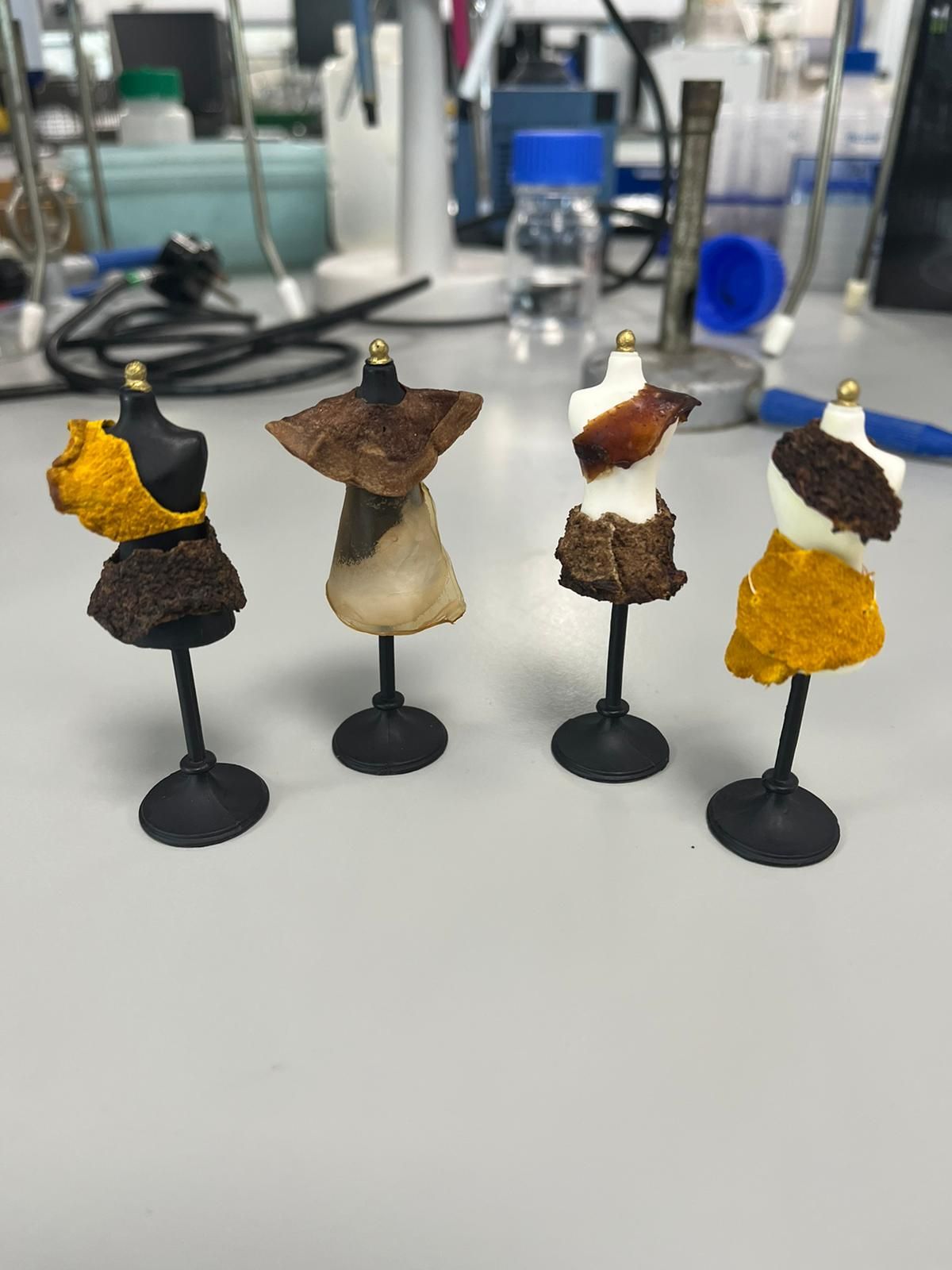 Four small dress forms wearing pieces of dried bacterial cellulose in yellow, brown and translucent tones