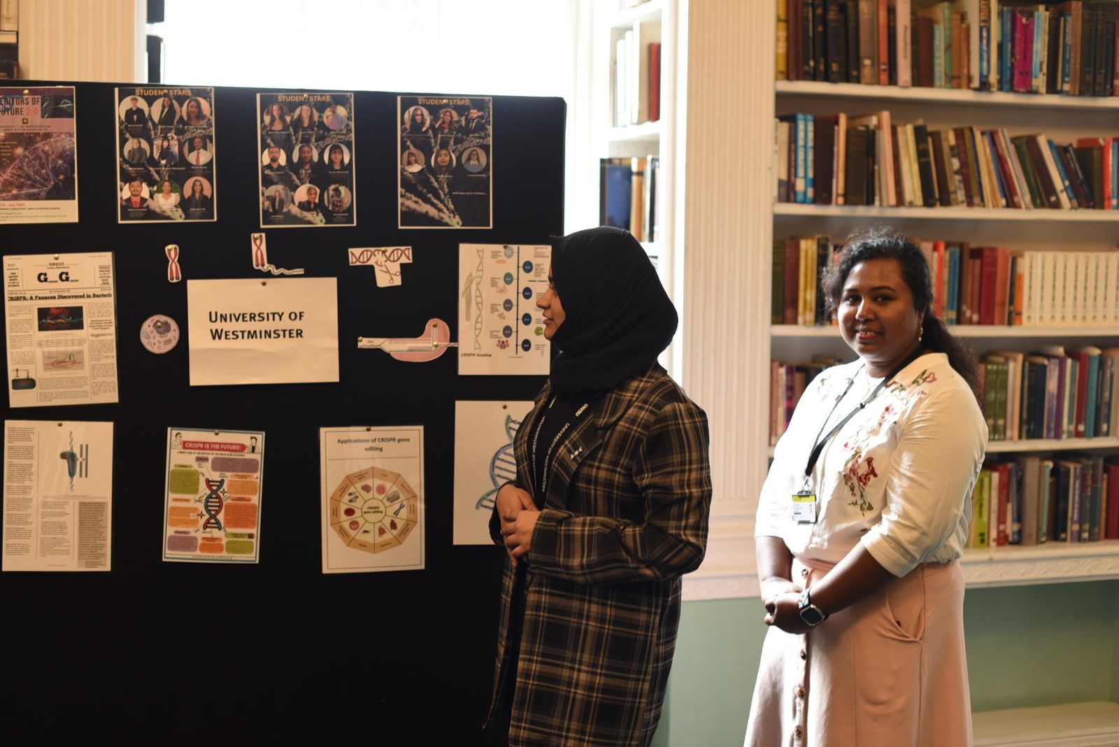 Subaiba and a colleague beside a display board of CRISPR posters and student profiles under a University of Westminster sign