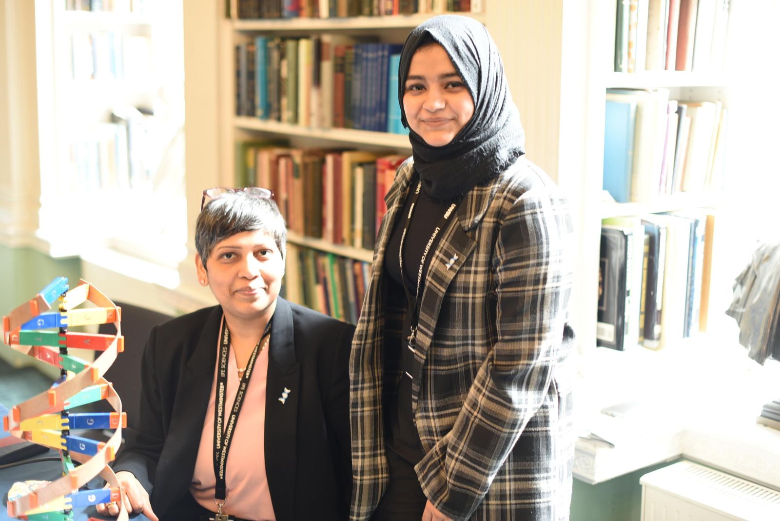 Subaiba standing beside Dr Kalpana Surendranath, who is seated next to a large DNA model in a library room