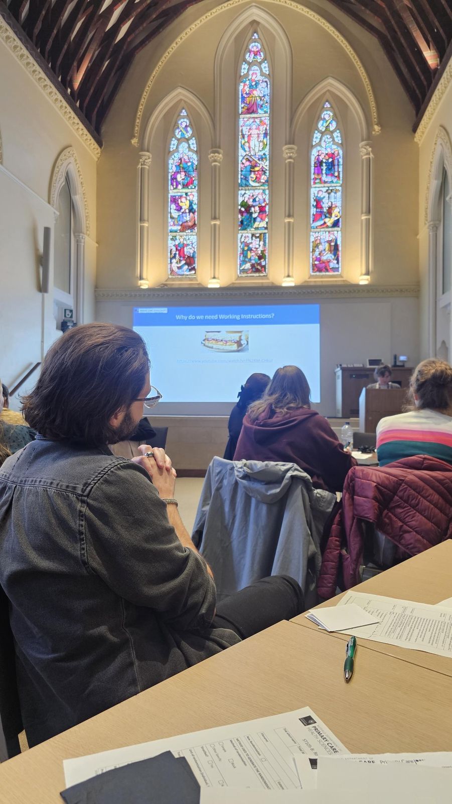 Course participants at desks facing a slide titled Why do we need Working Instructions, under stained-glass windows