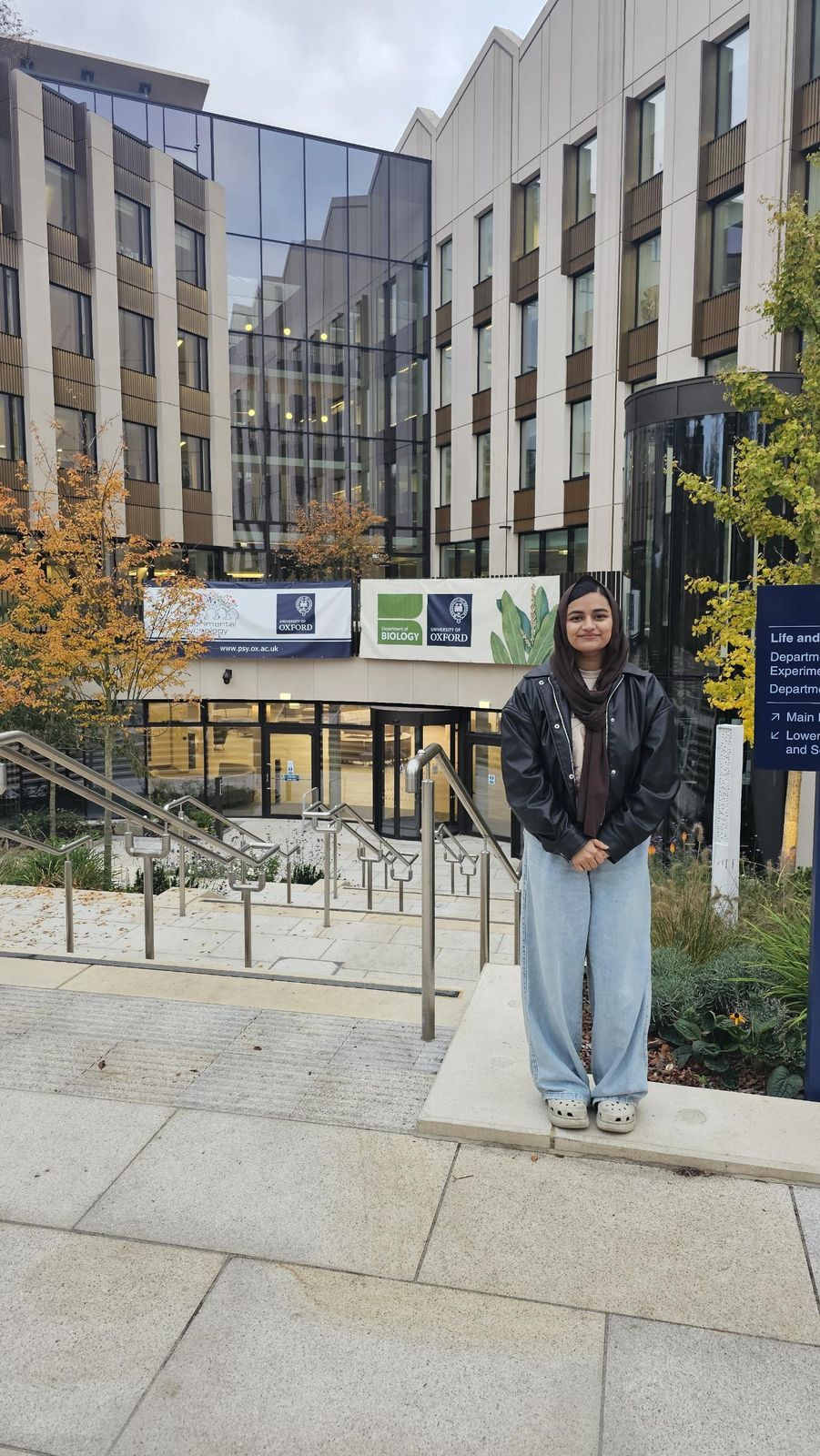Subaiba standing outside a modern building with Department of Biology and Experimental Psychology banners